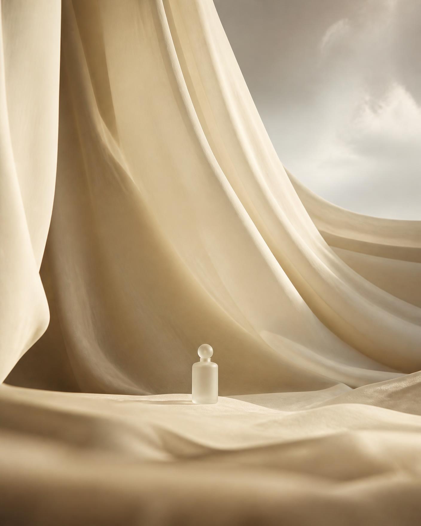A single frosted bottle inside a monumental landscape of pale fabric